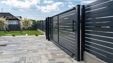 A modern panel fence in anthracite color, visible sliding gate to the garage and a slab driveway.